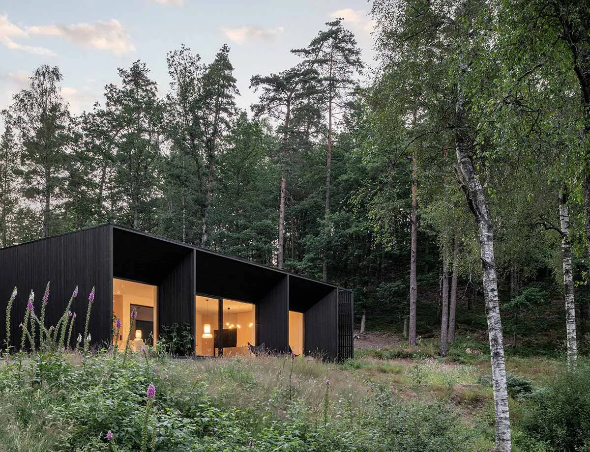 A modern residential building with wooden exterior surrounded by trees and flowers.