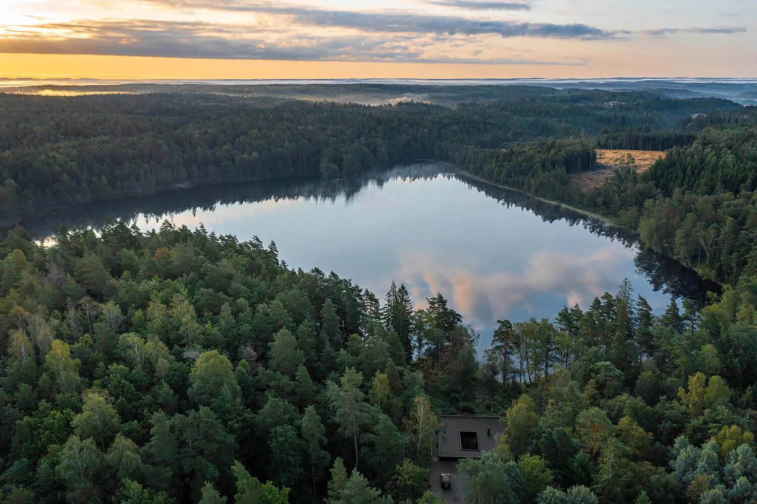 A serene landscape featuring a tranquil lake surrounded by dense forests at sunset.