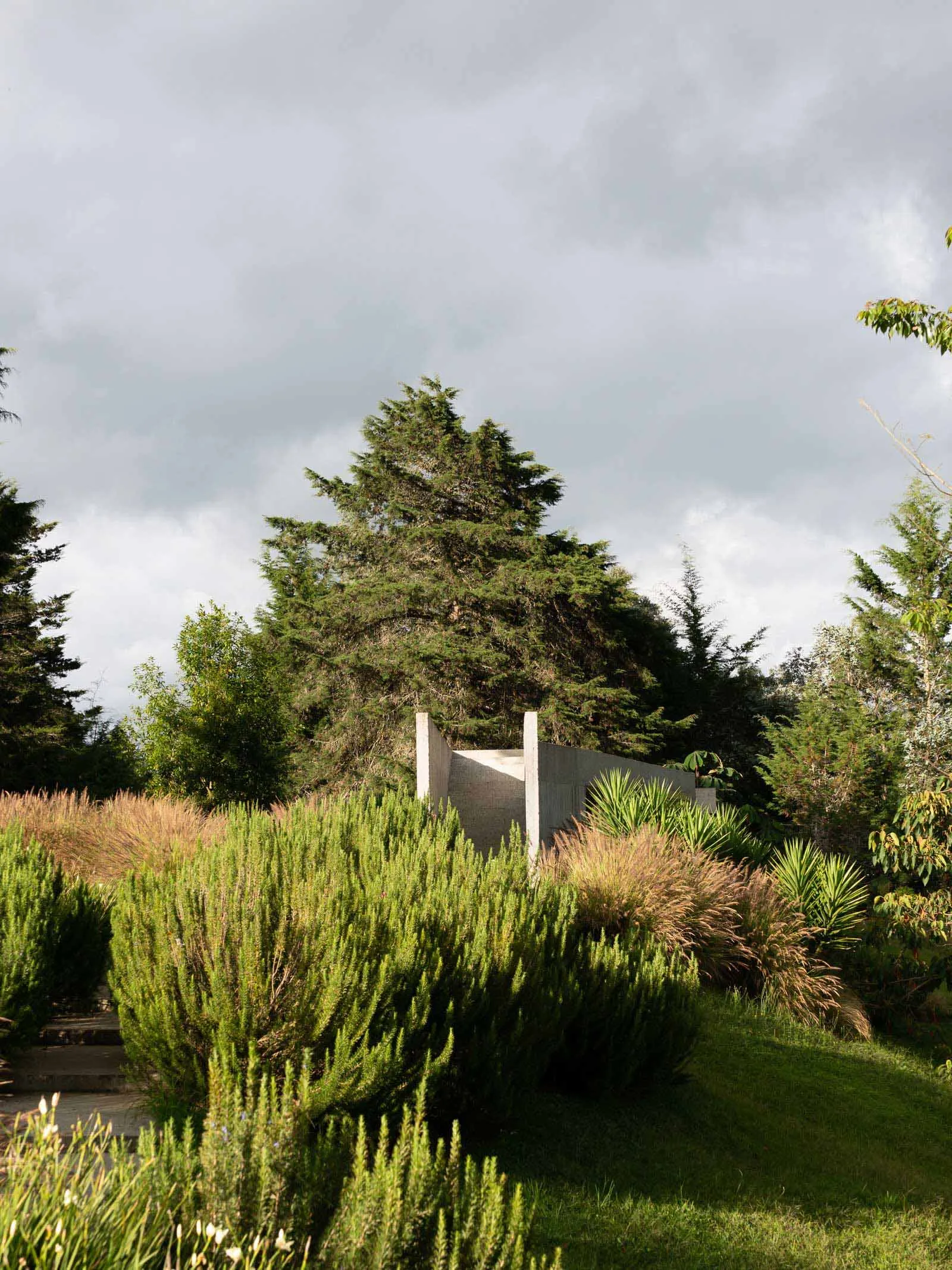 A modern landscape featuring a concrete structure surrounded by greenery and trees under a cloudy sky.