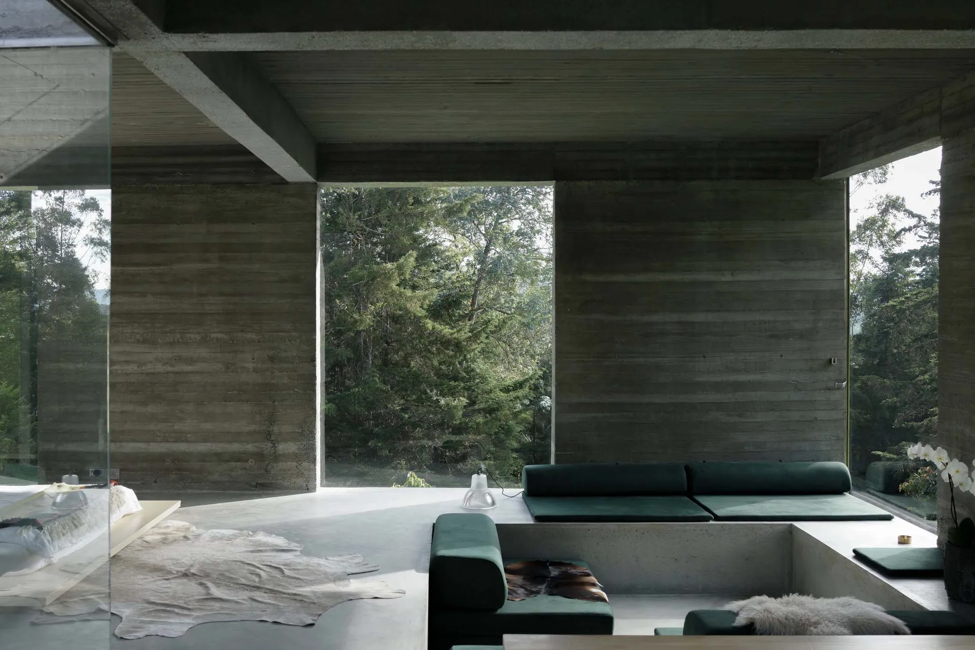Modern minimalist living room with concrete walls, floor, and ceiling, featuring a green lounge area.