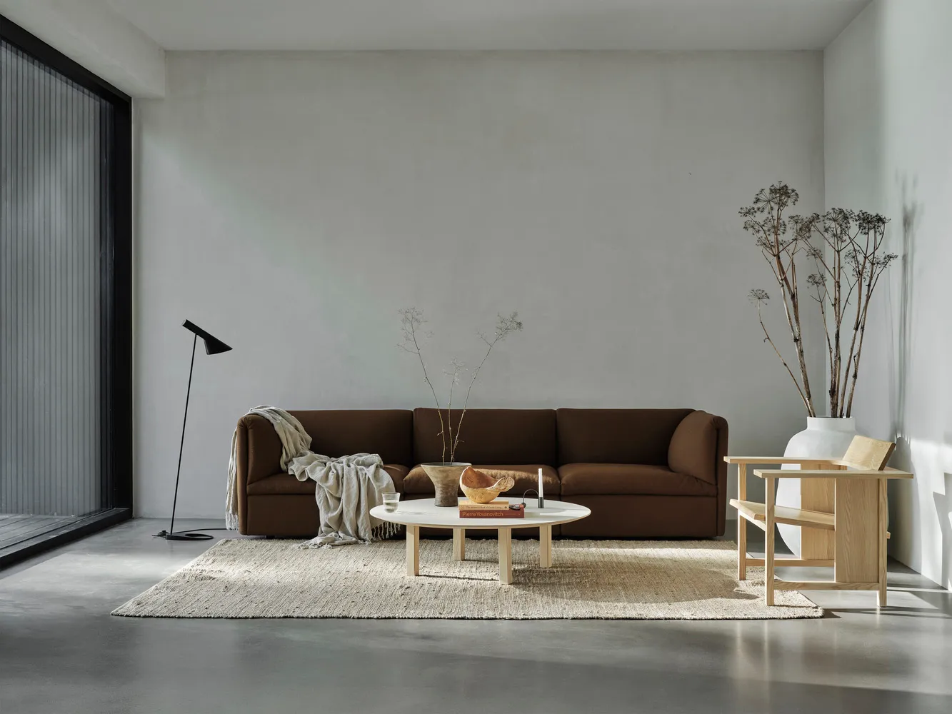 Modern minimalist living room featuring a brown sofa, white coffee table, and concrete floor and walls.