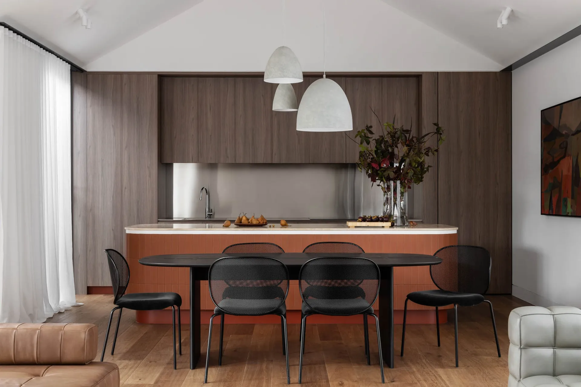 A modern residential kitchen with wood cabinets, a stainless steel backsplash, and a black dining table with black chairs.
