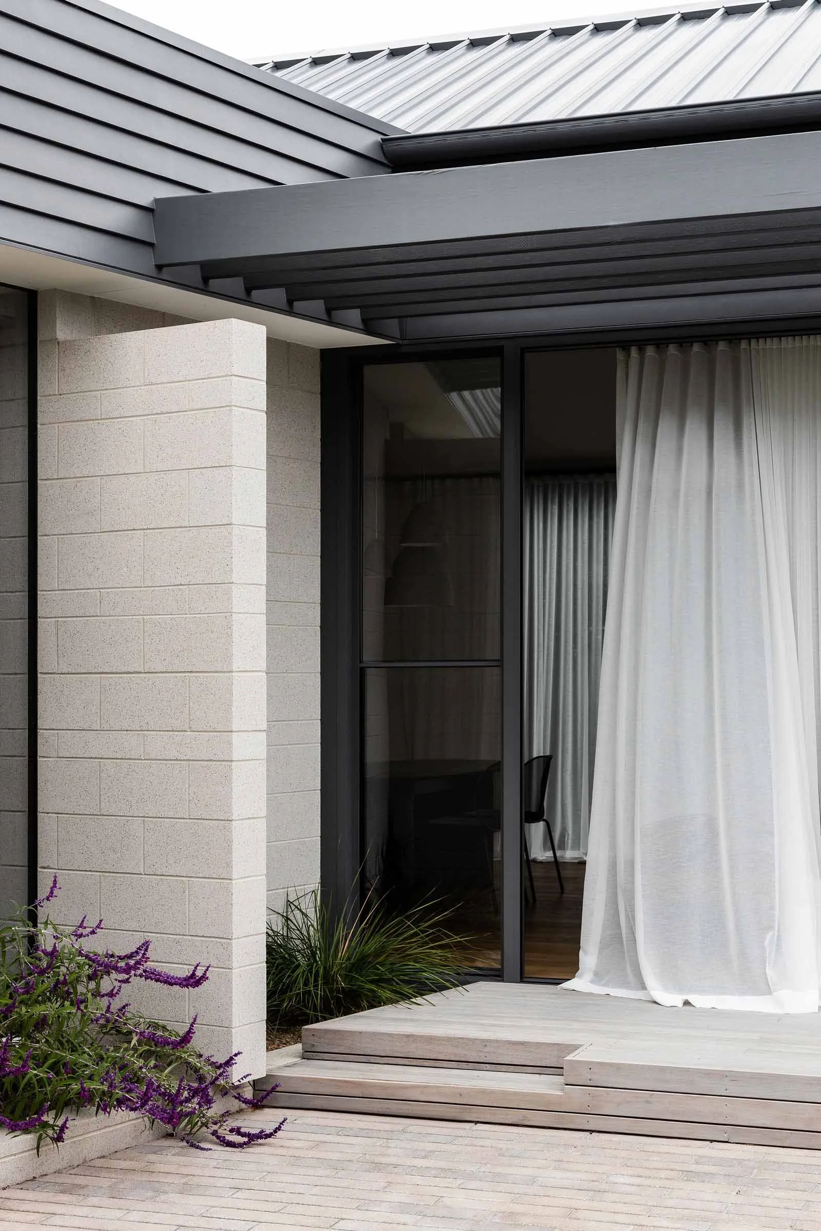 A modern house entryway with a concrete column and wooden deck, featuring sheer curtains.