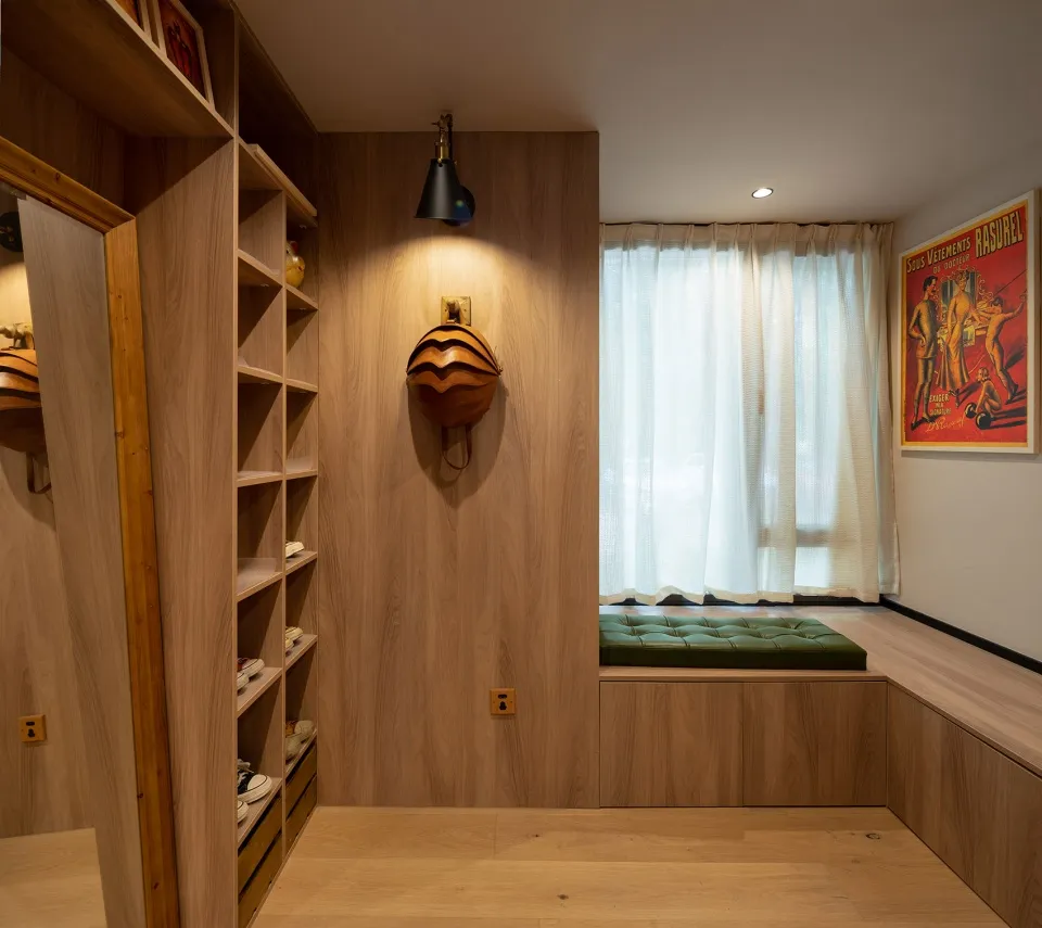A modern closet with wooden shelves and a window seat with green cushions.