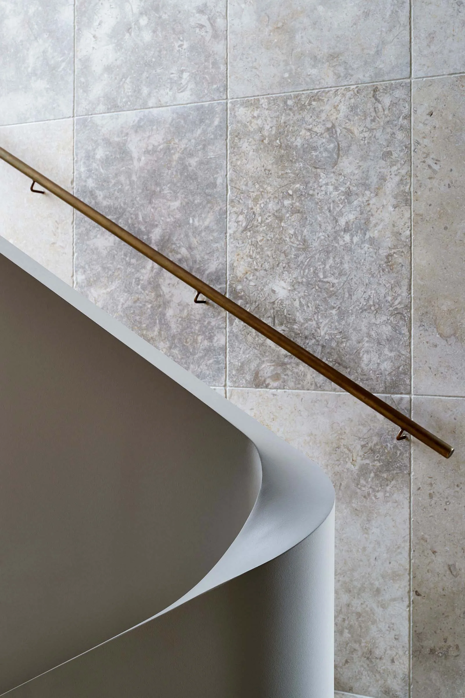 A modern staircase featuring a bronze metal railing against a textured wall.