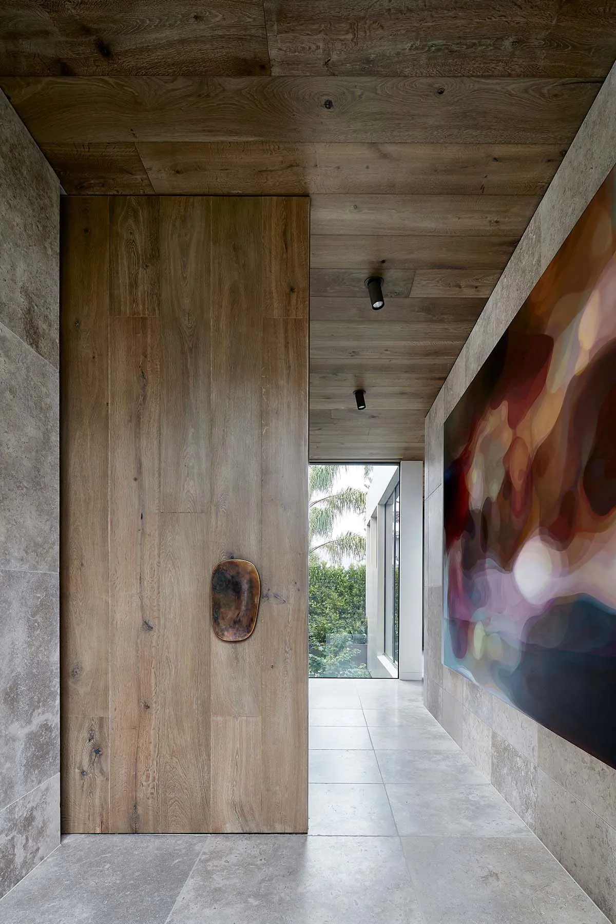 A minimalist entryway with a wooden door, concrete floor, and abstract art painting.