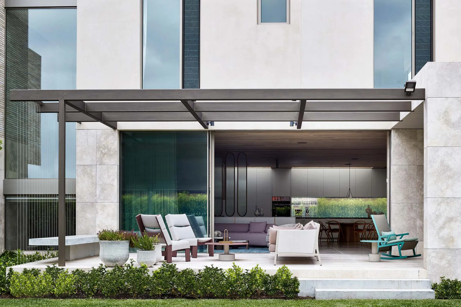 Modern concrete patio featuring a pergola, plants, and outdoor furniture under a shaded area.