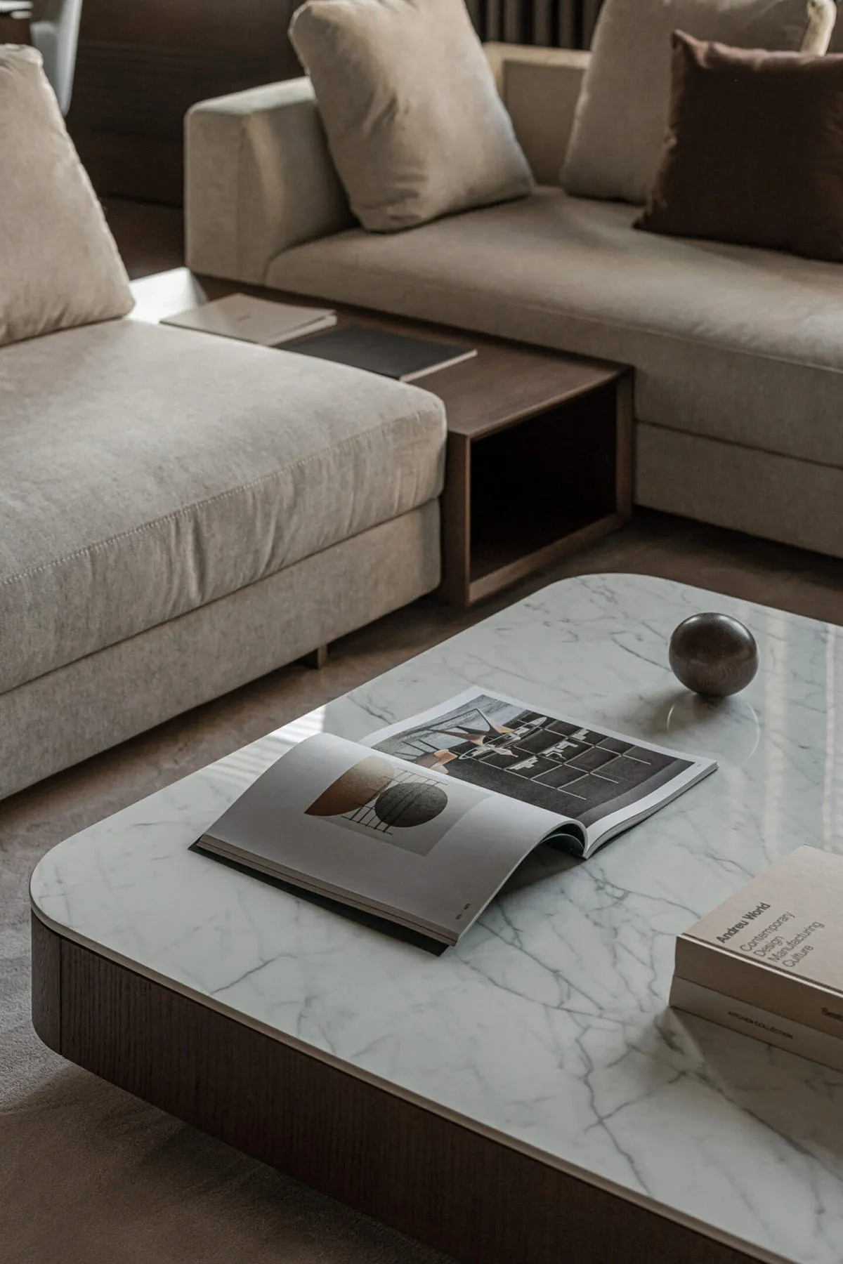 Modern living room with beige sofas, marble coffee table, and books.