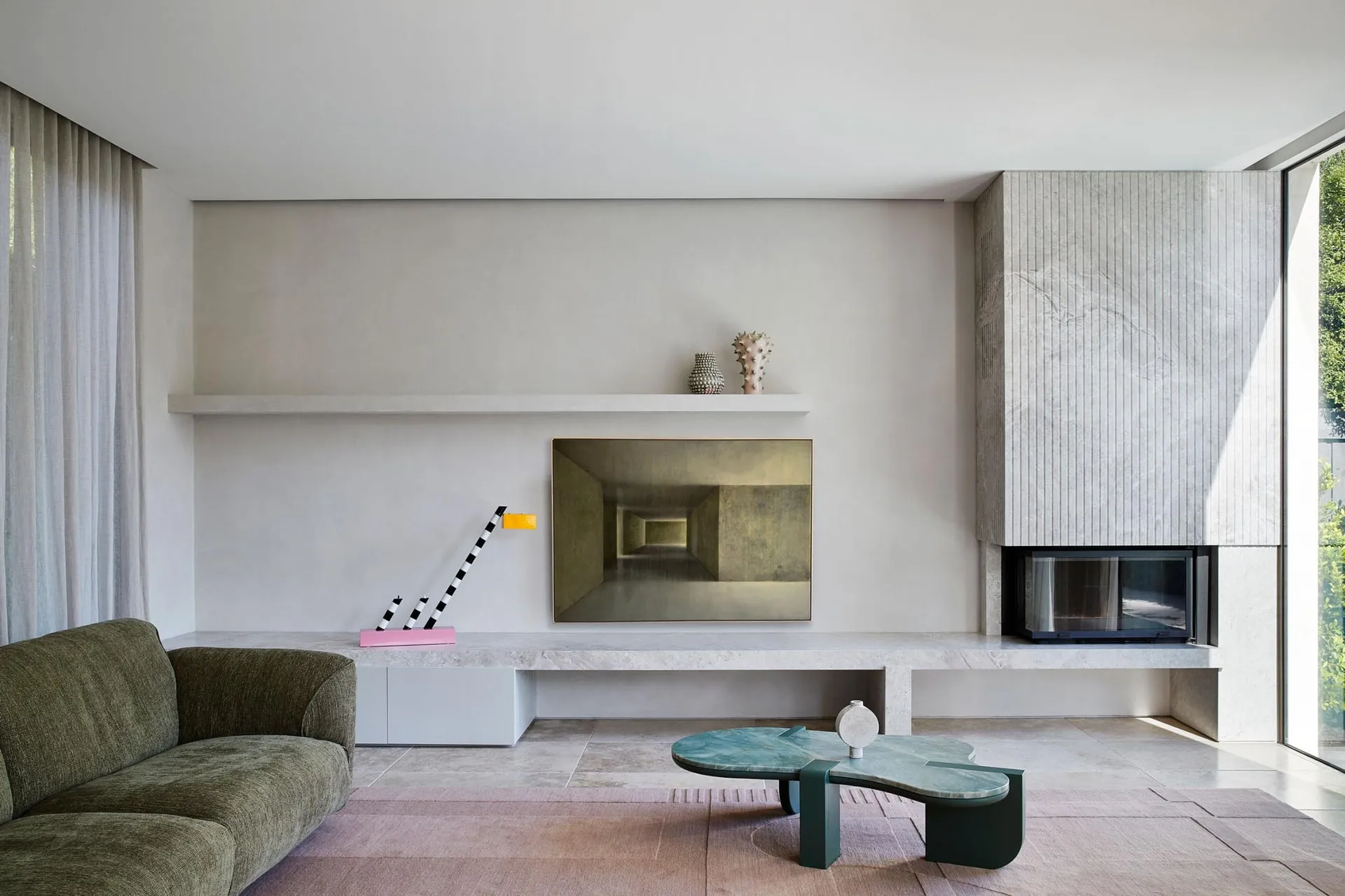 A minimalist living room with a concrete fireplace, large windows, and a simple sofa.