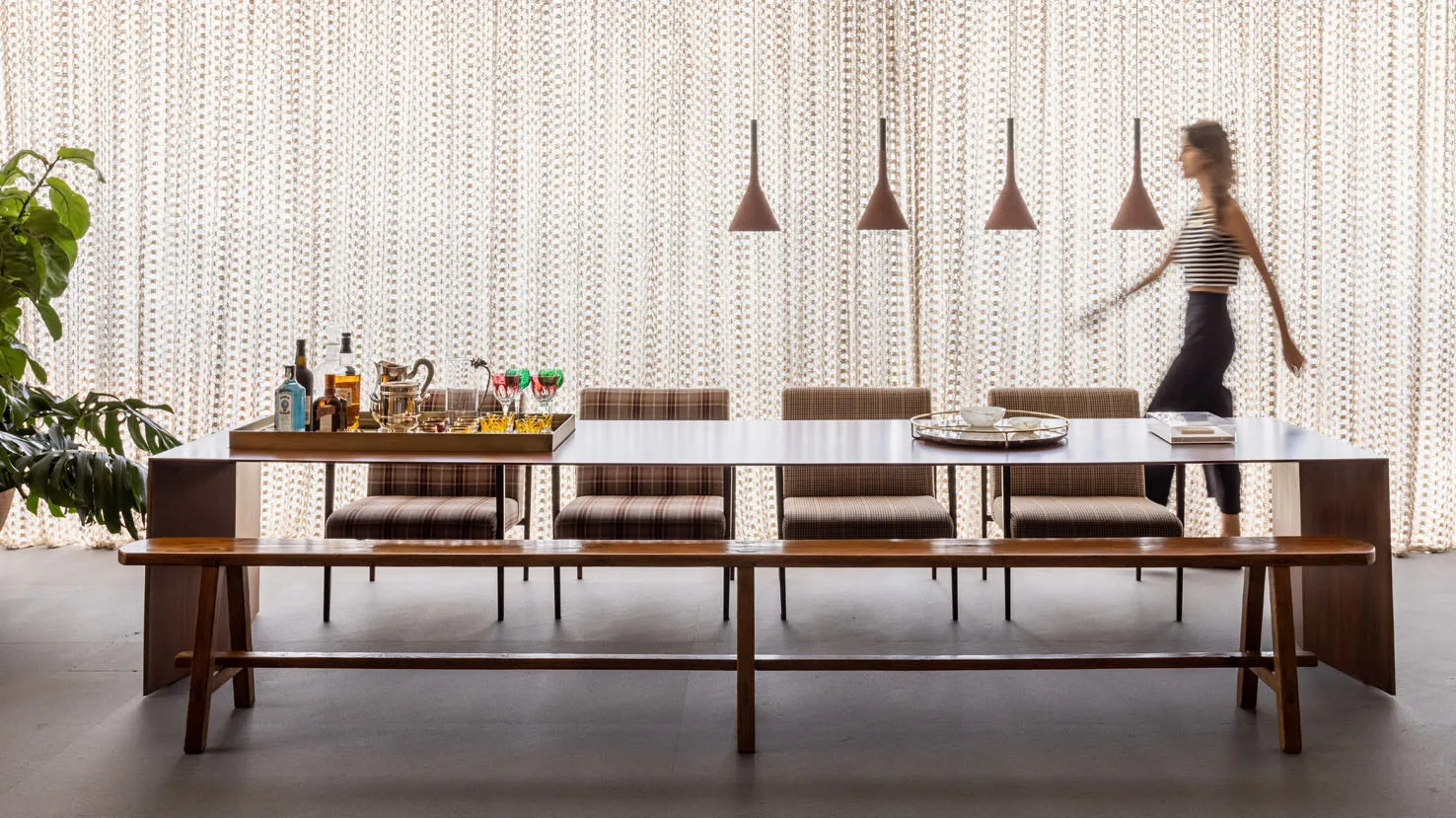 A contemporary restaurant dining room featuring wooden furniture, upholstered seats, and glass pendant lights.