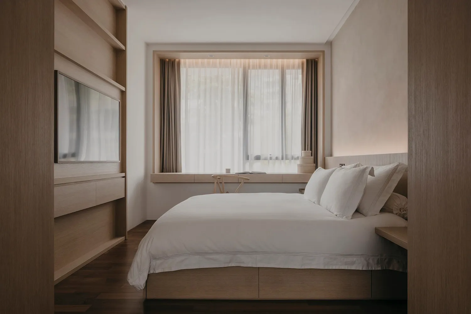 Modern minimalist bedroom with a large window, white bedding, and wood furniture.