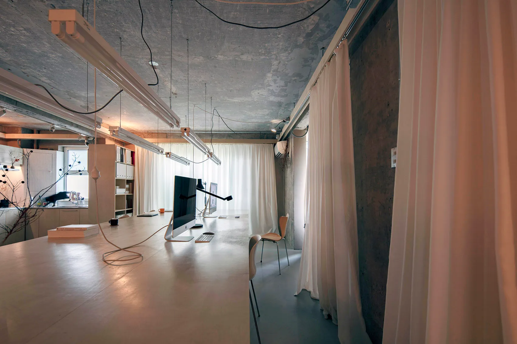 A modern office space with concrete walls and white curtains.
