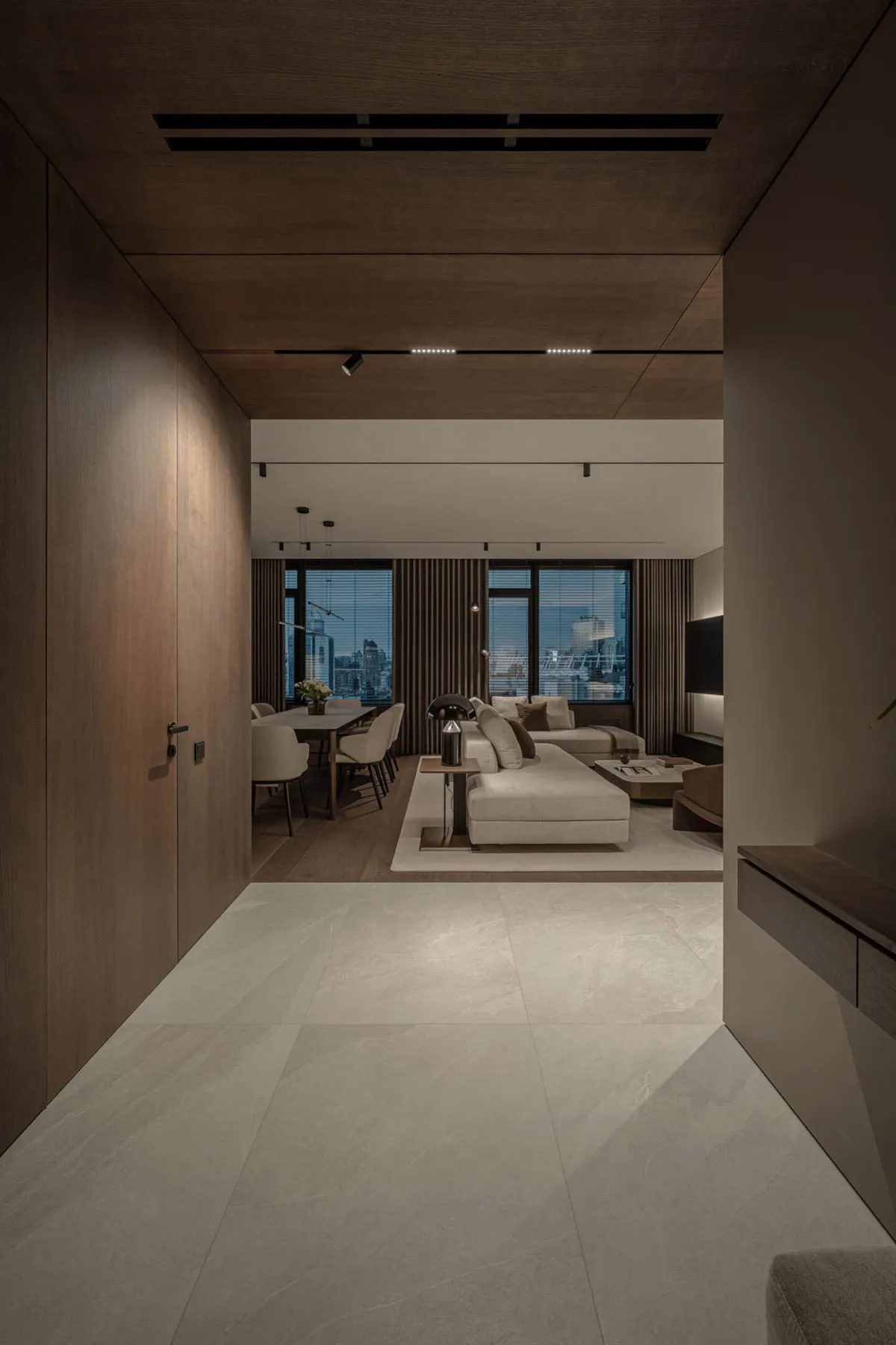 A modern living and dining room with a white marble floor, wooden accents, and large windows overlooking a cityscape.
