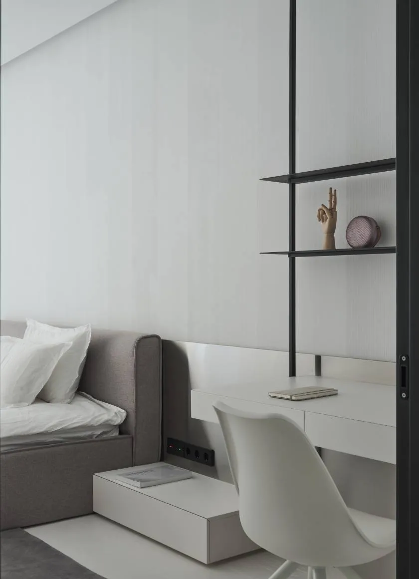 A minimalist bedroom with a white bed, floating desk, and open shelves.