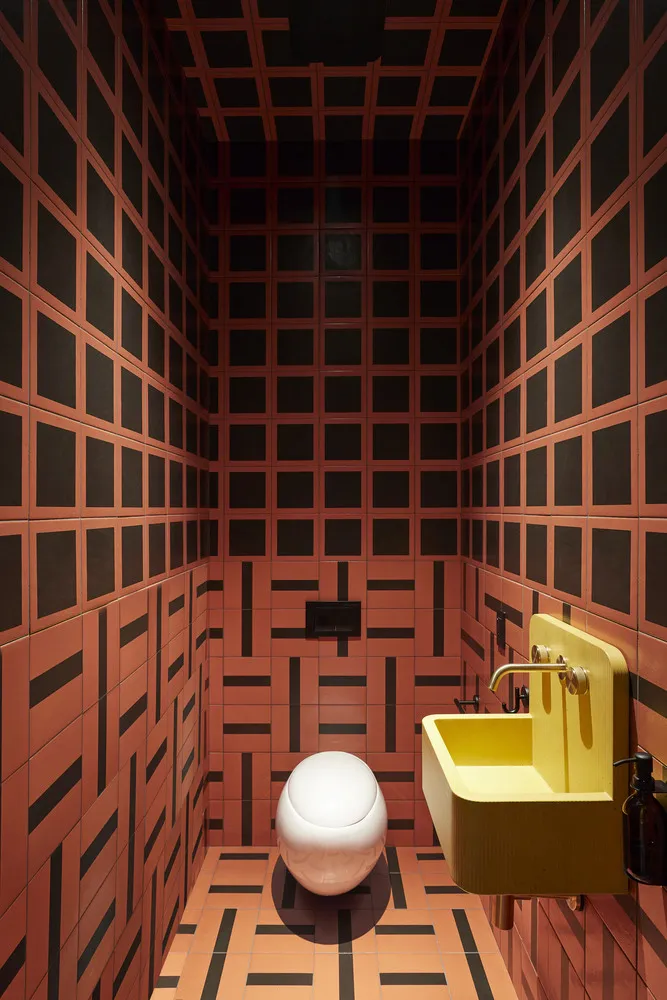 A modern industrial bathroom with a striking patterned tile design, featuring a contemporary toilet and a vibrant yellow sink