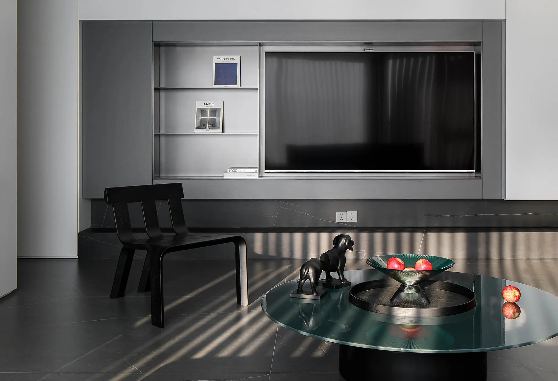 Contemporary living room featuring dark metallic furniture, a sleek glass coffee table, and a minimalist bookshelf.