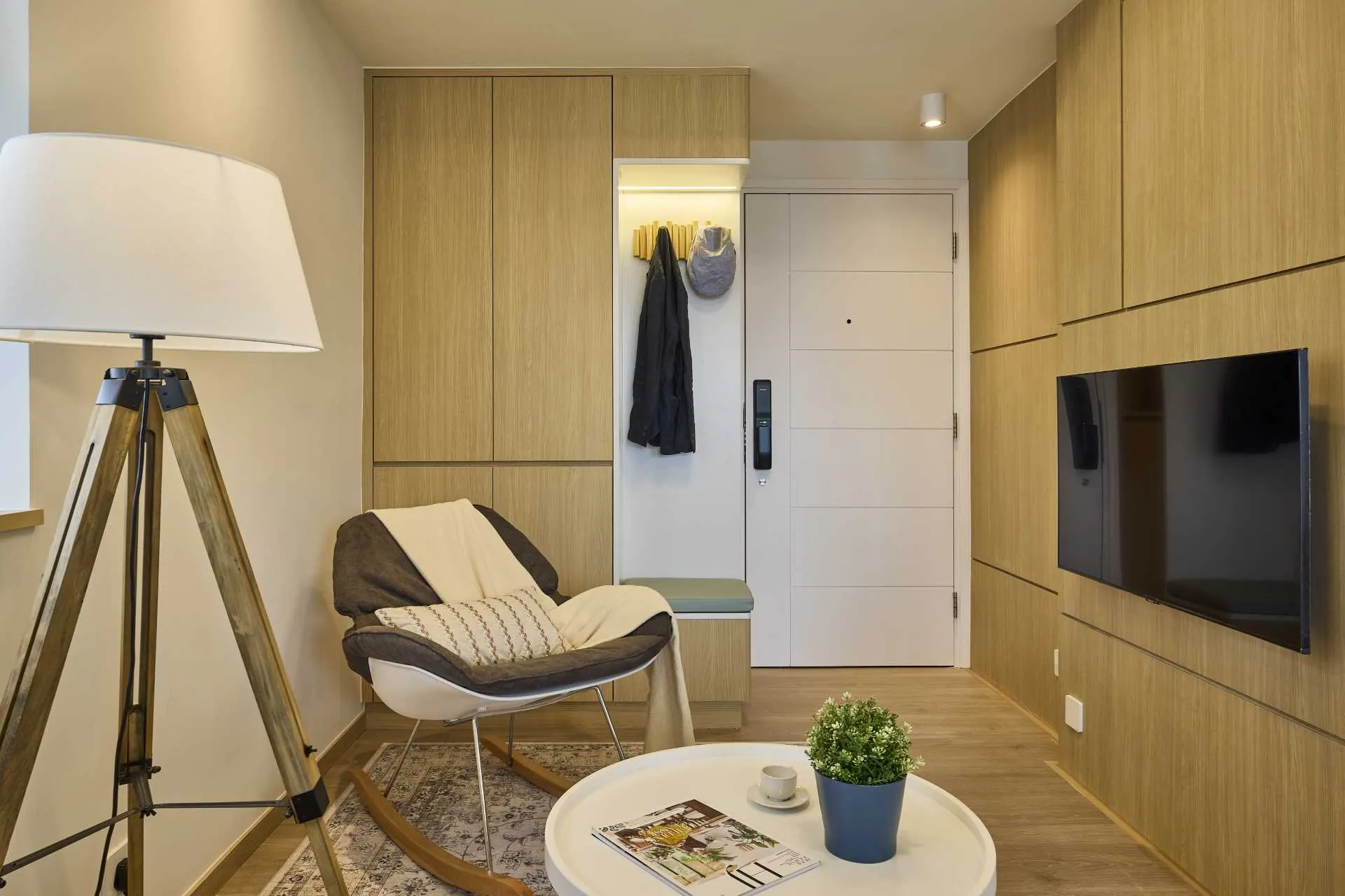 A modern apartment living room with wood flooring, wooden furniture, and a cozy rocking chair. Features a flat-screen TV, a w