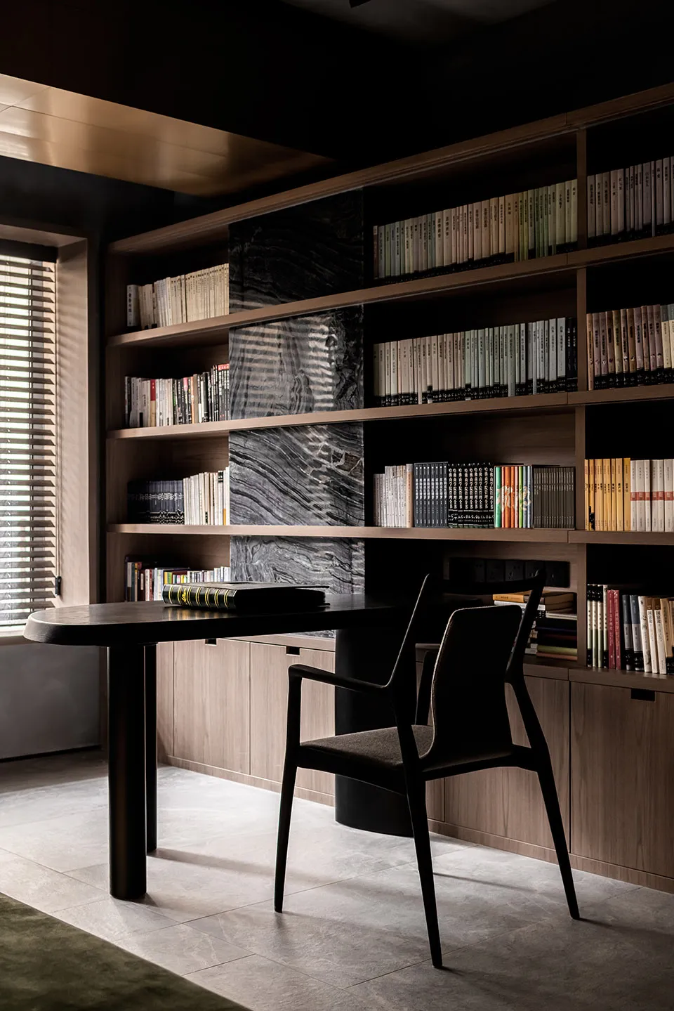 A modern study room featuring a sleek, black wooden desk and a large wooden bookshelf filled with books arranged neatly. The