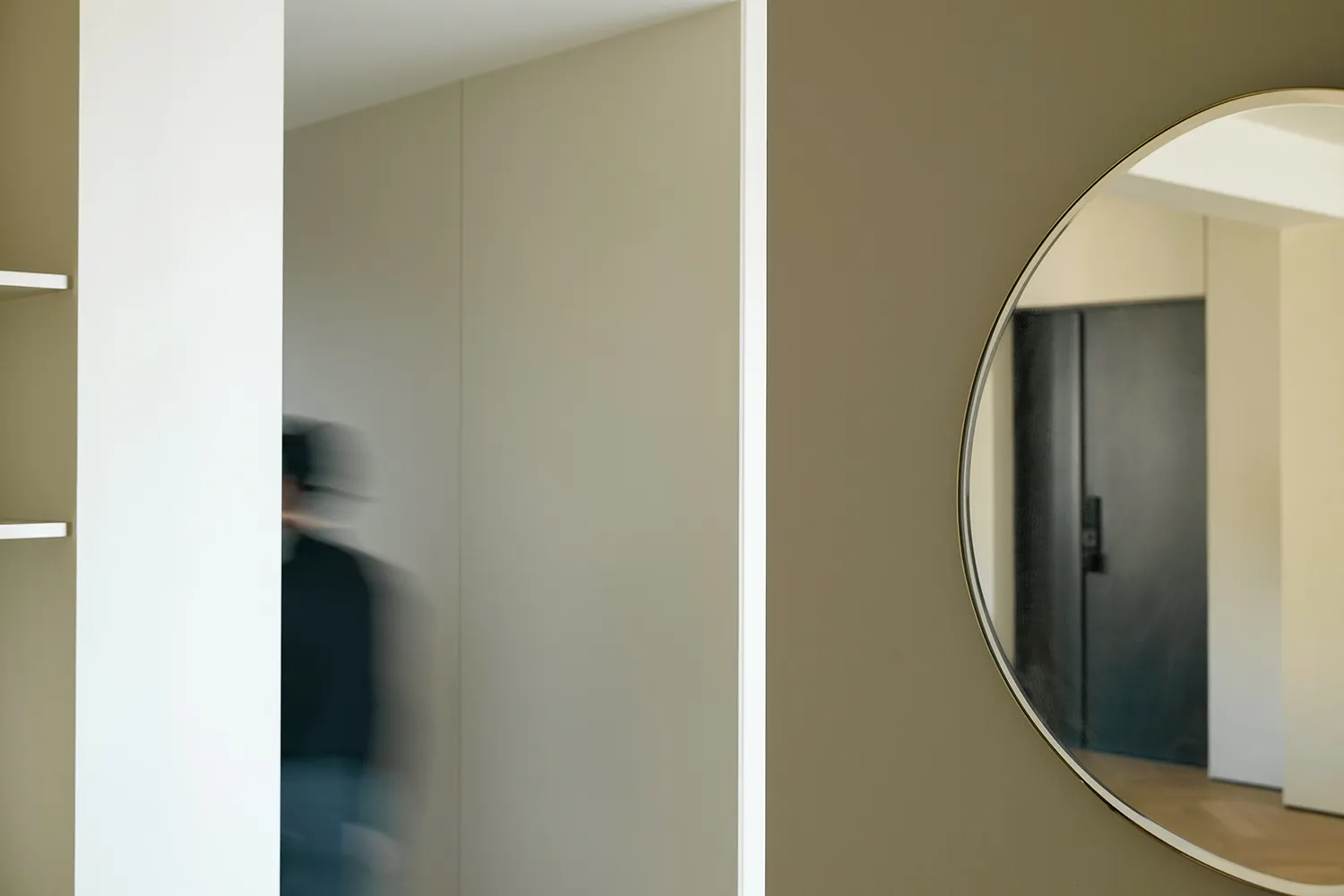 A minimalist interior featuring a person in a suit walking through a hallway with light-colored walls and flooring.