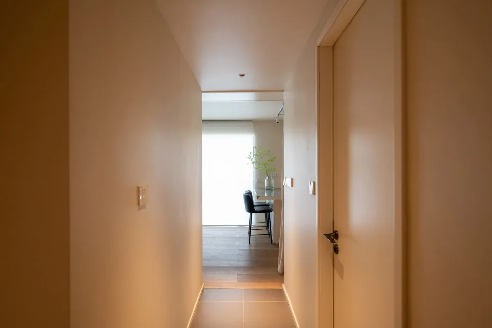 A modern corridor featuring minimalist concrete tiles on the floor, leading towards a dining area with a black chair and flor
