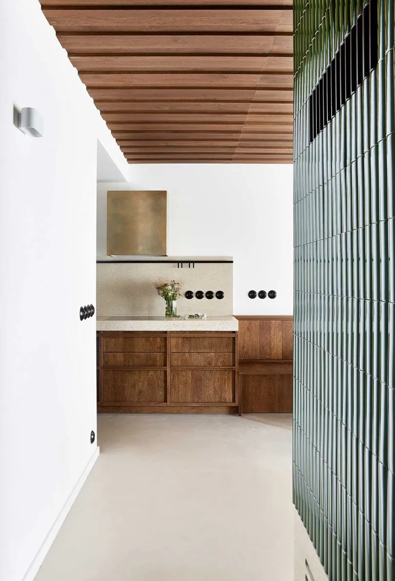 A modern kitchen interior with marble countertops, concrete backsplash, and wooden cabinets.