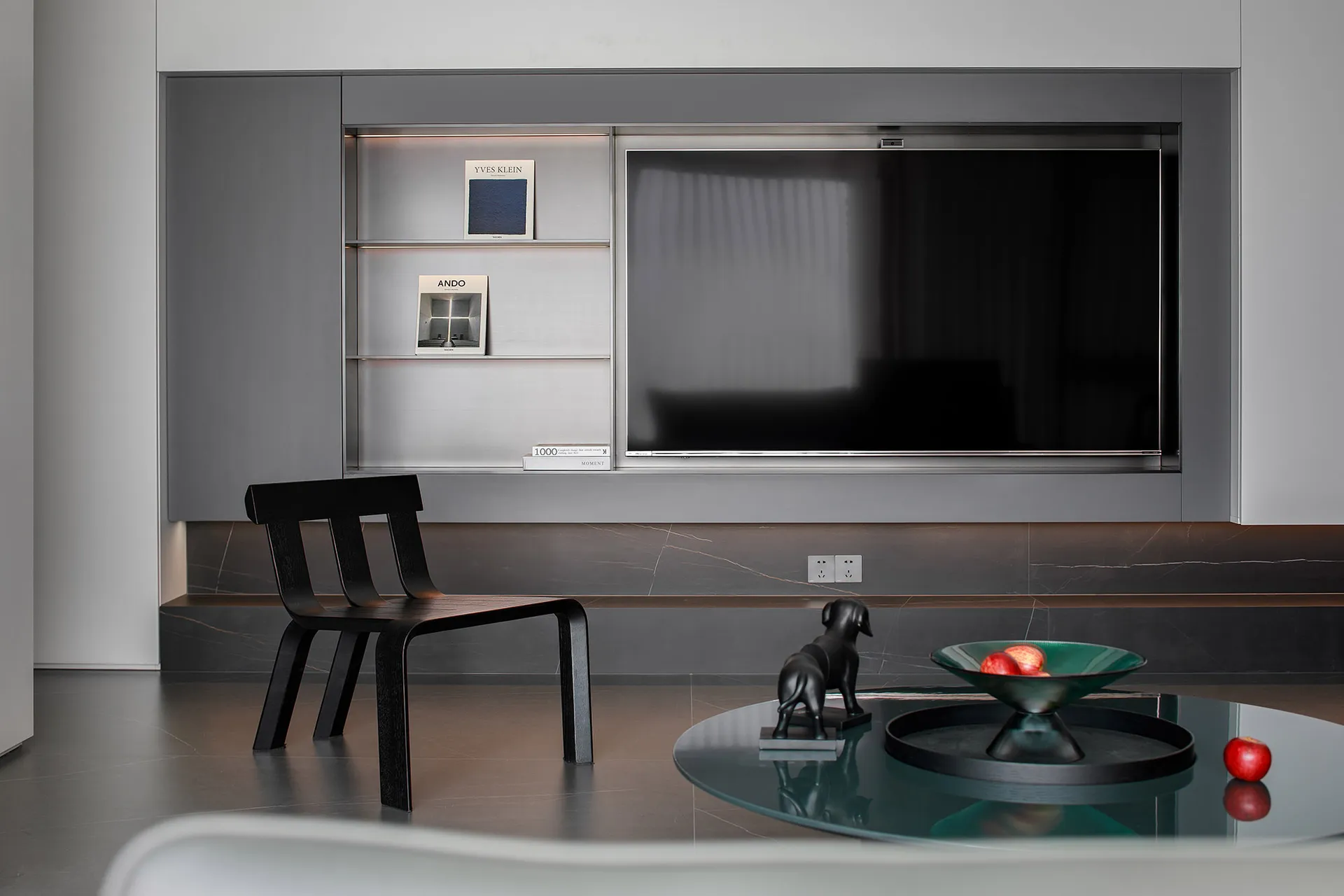 A modern living room featuring a metallic black dining chair on a polished concrete floor against a metallic black wall.