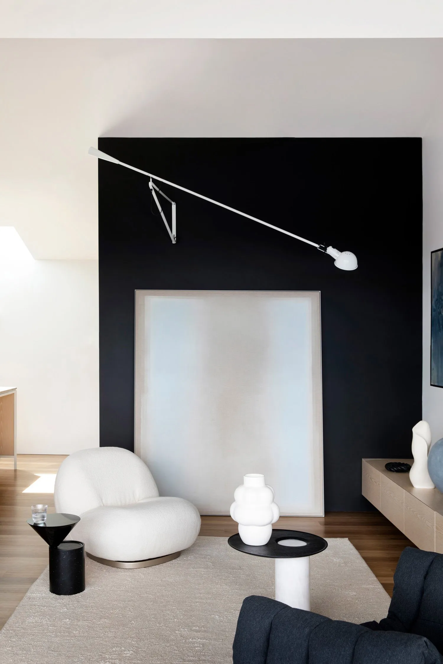 A modern living room with white leather furniture, minimalist decor, and a black accent wall.