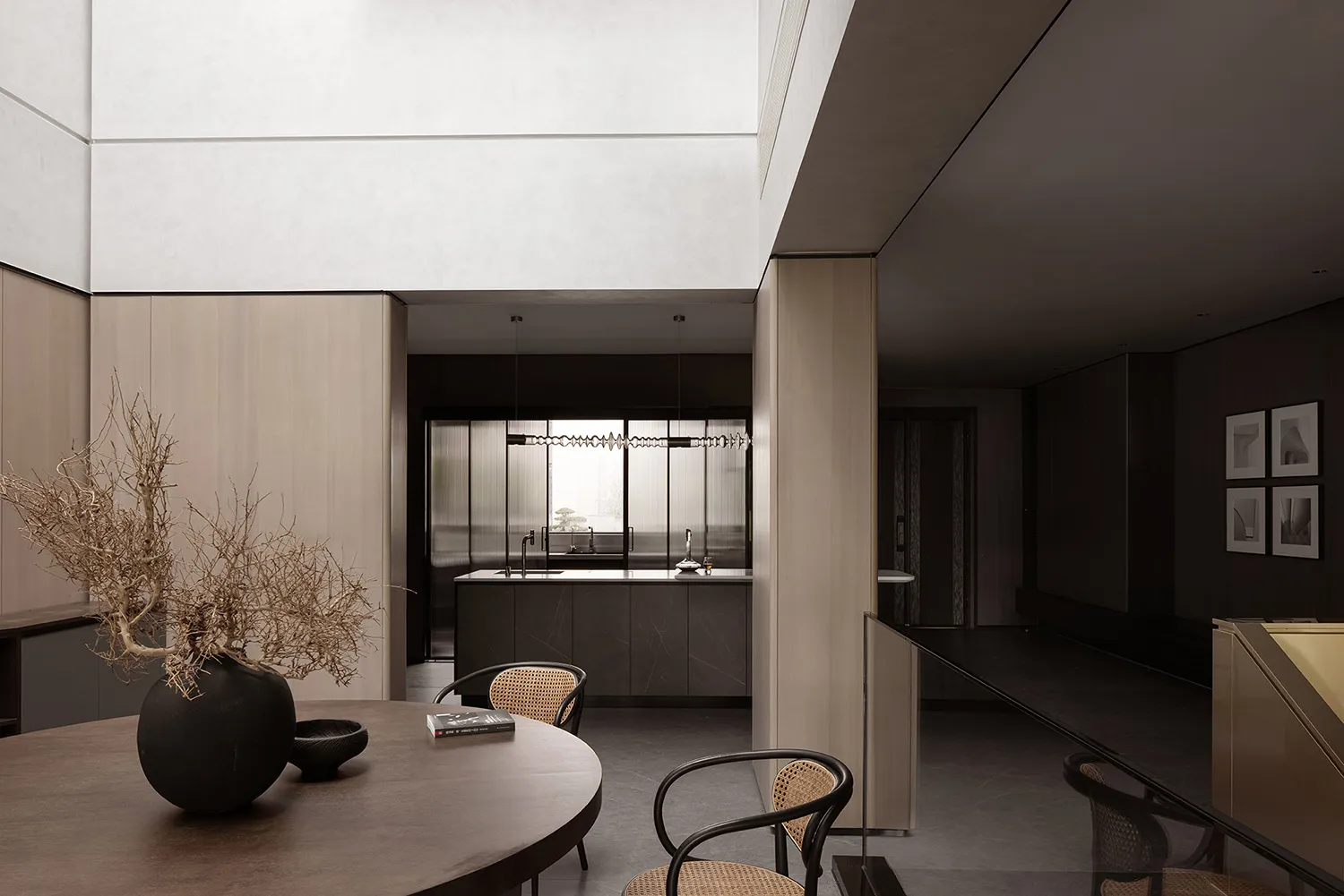 A minimalist kitchen with natural wood cabinets and concrete countertops, featuring a round dining table with chairs and a va
