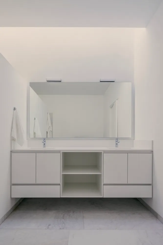 Modern minimalist bathroom with white walls, sink, and cabinets.