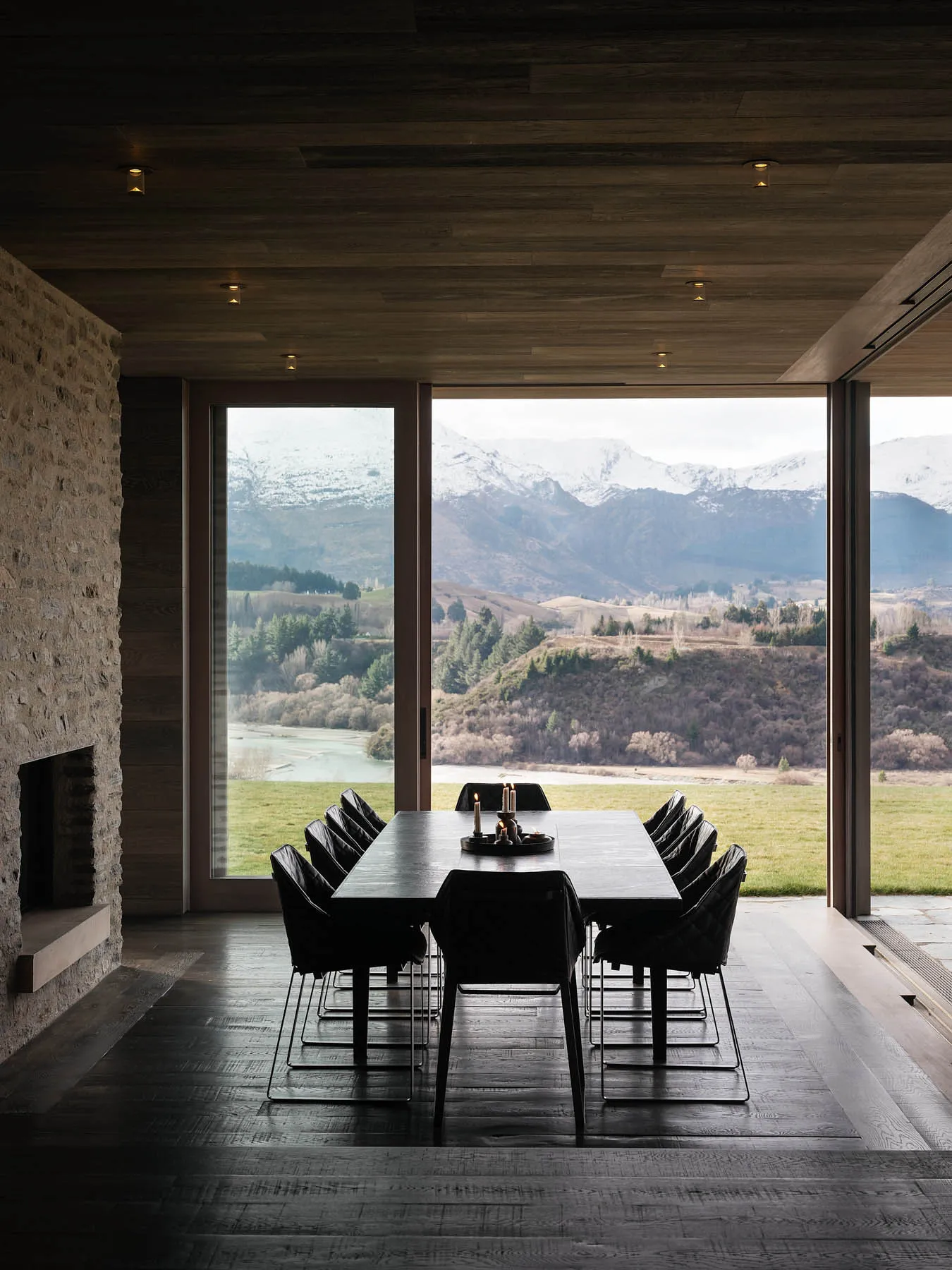 An elegant dining room with large windows showcasing a picturesque mountain landscape, featuring modern black wooden table an