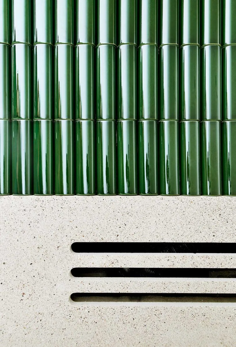 Green tiled wall with a white concrete base featuring horizontal slits.