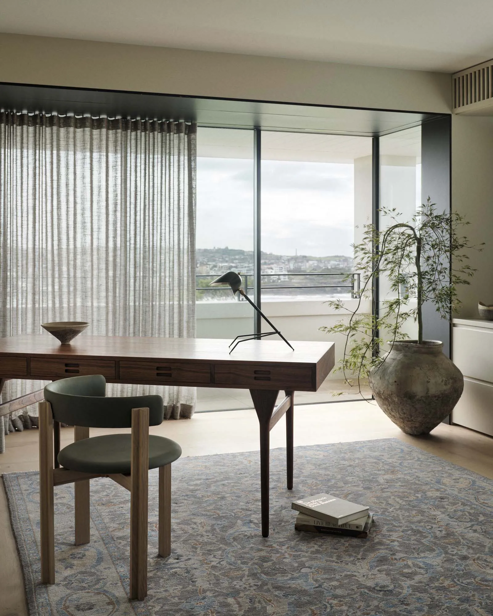 A modern home office with a wooden desk, green chair, and large window overlooking a city.