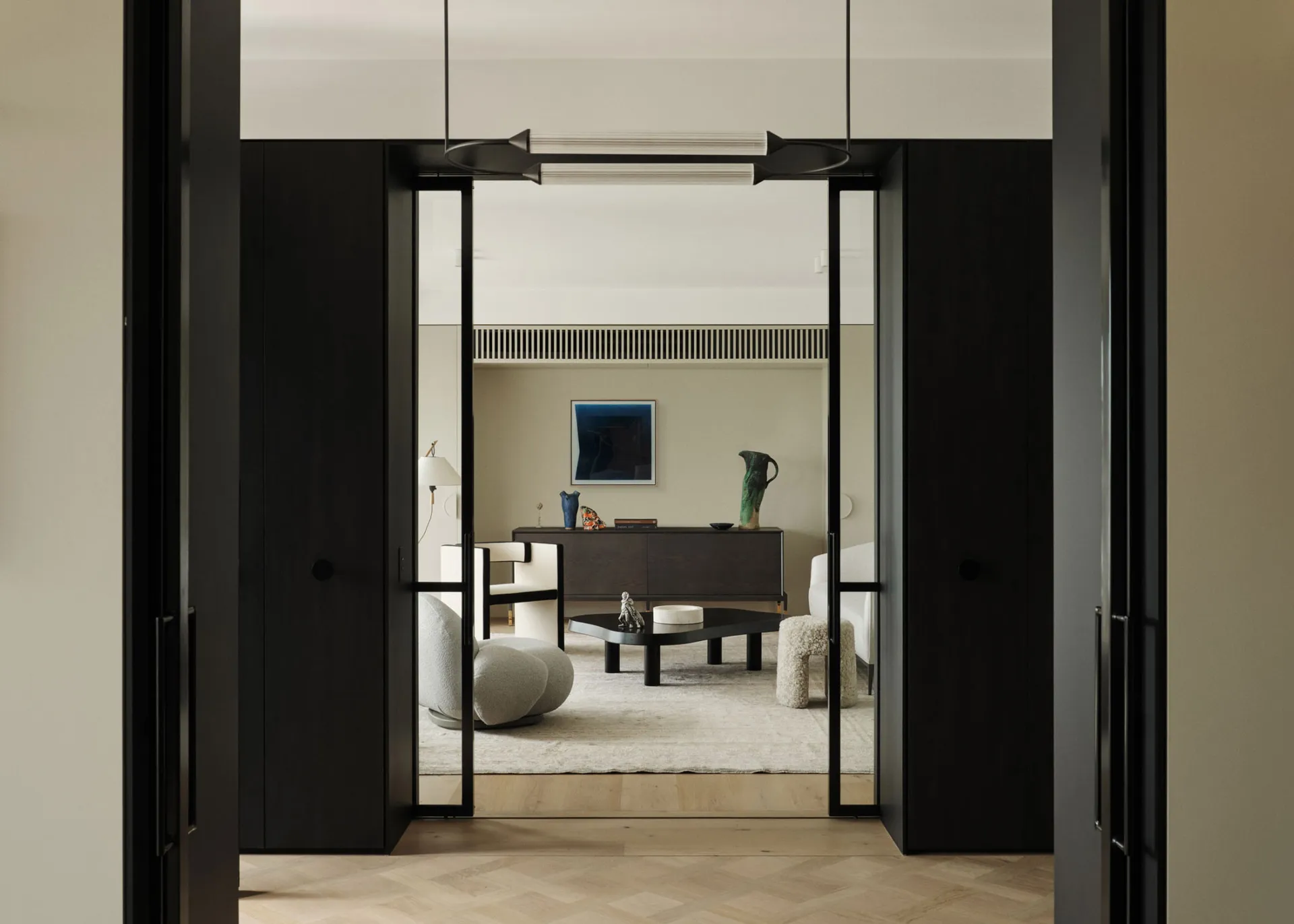 Modern living room with black frame door, white and dark wood furniture, and minimalist decor.