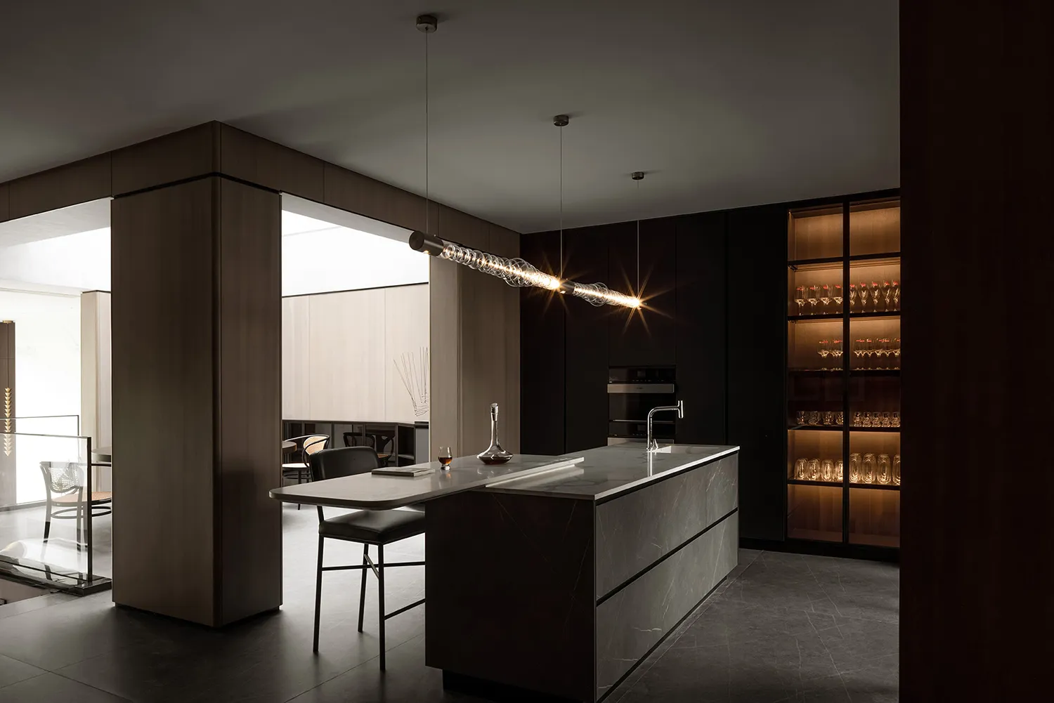 Modern minimalist black kitchen with marble countertop and pendant lighting.