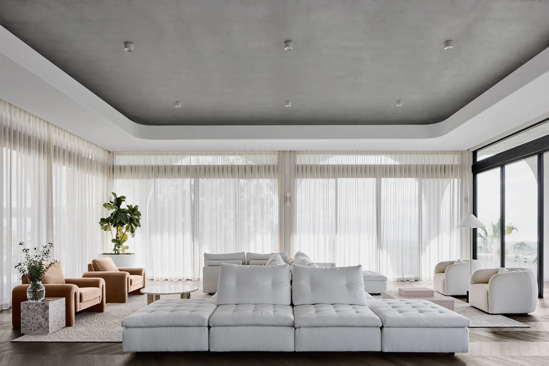 Modern minimalist living room featuring a large white fabric sofa, a beige armchair, and a glass coffee table, with large win