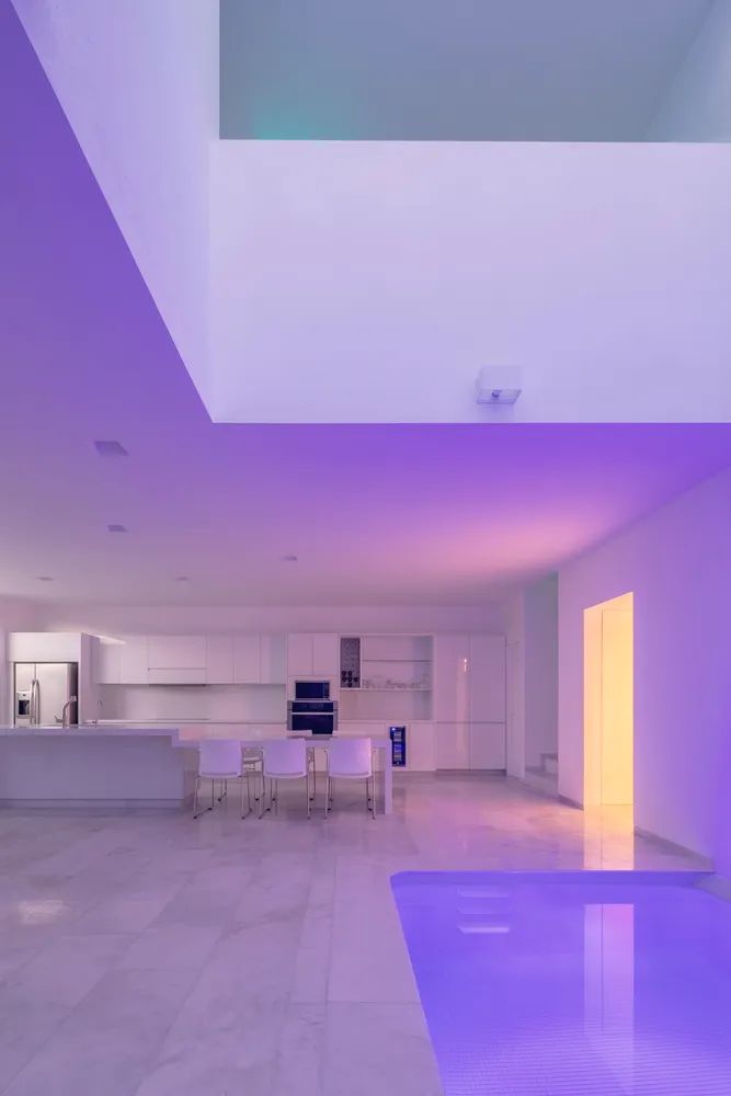 Modern minimalist kitchen with white marble countertops and a pool area with purple lighting.