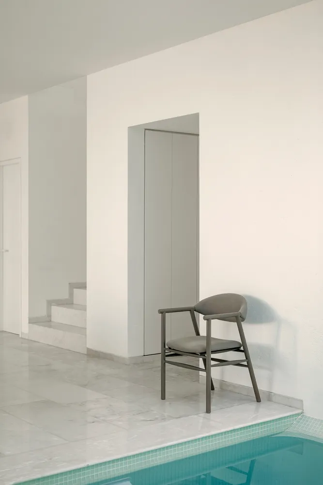 A minimalist modern chair made of marble stone, positioned next to a pool.