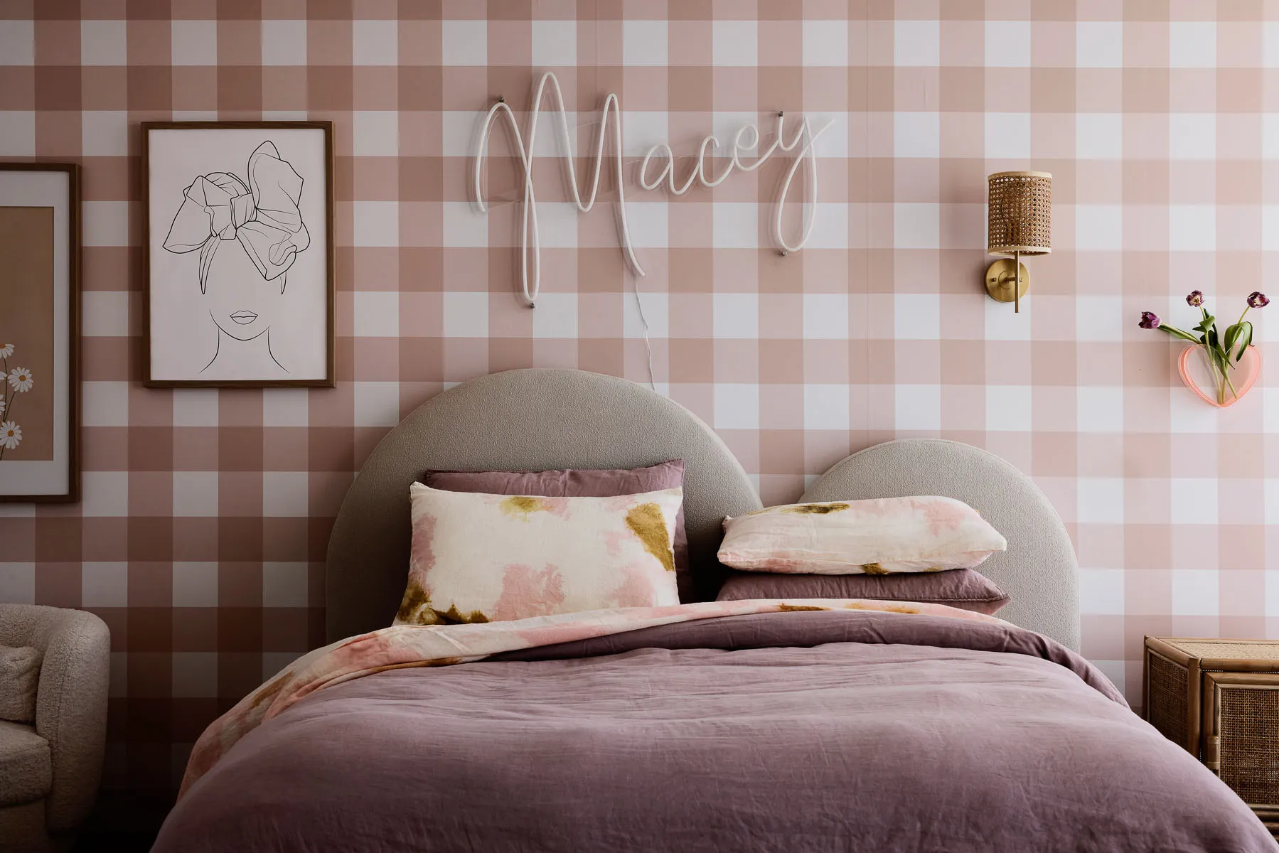 A minimalist bedroom featuring light pink and white checkered wallpaper, a cozy bed with floral-patterned cushions, and a han