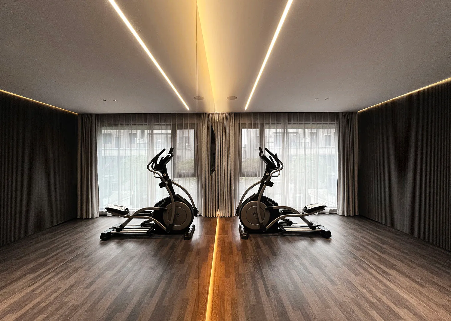 Fitness room with two elliptical machines, wood flooring, and large windows.