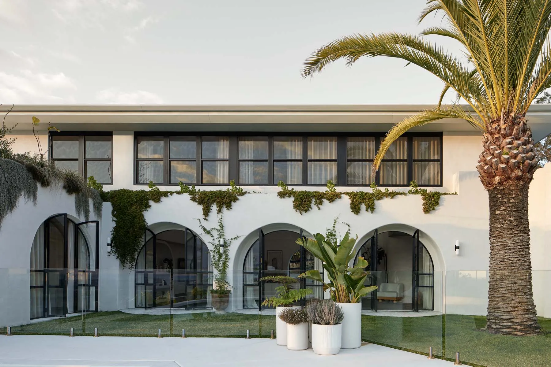 Modern residential exterior with white render, greenery, and palm trees.