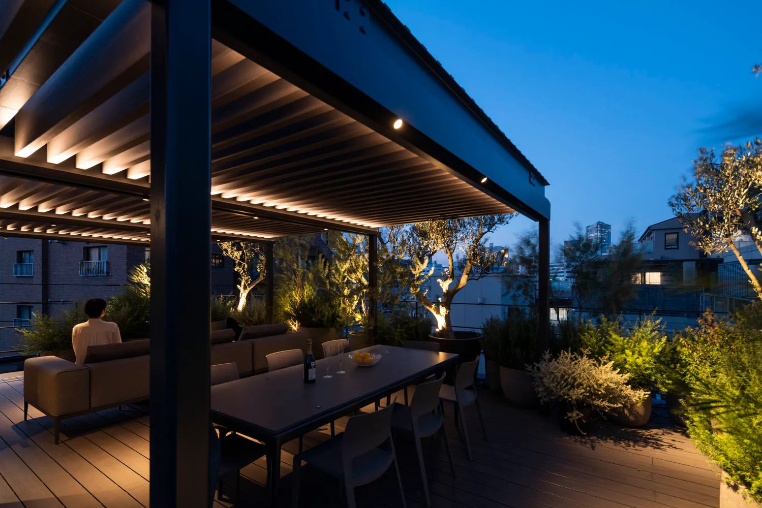 A modern, minimalist rooftop patio with concrete flooring, metal furniture, and LED lighting features.