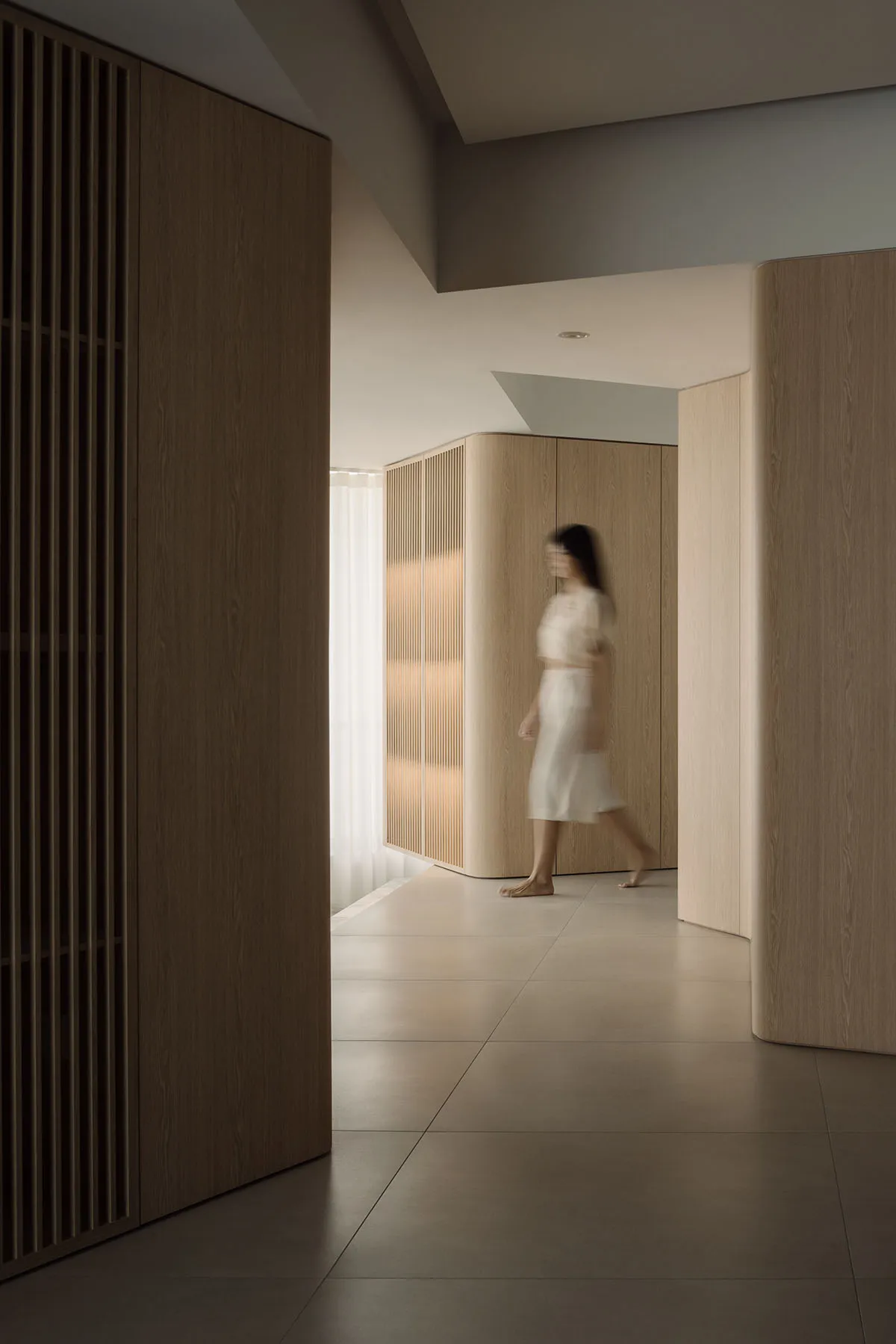 A minimalist interior space with wooden walls and a person walking through it.