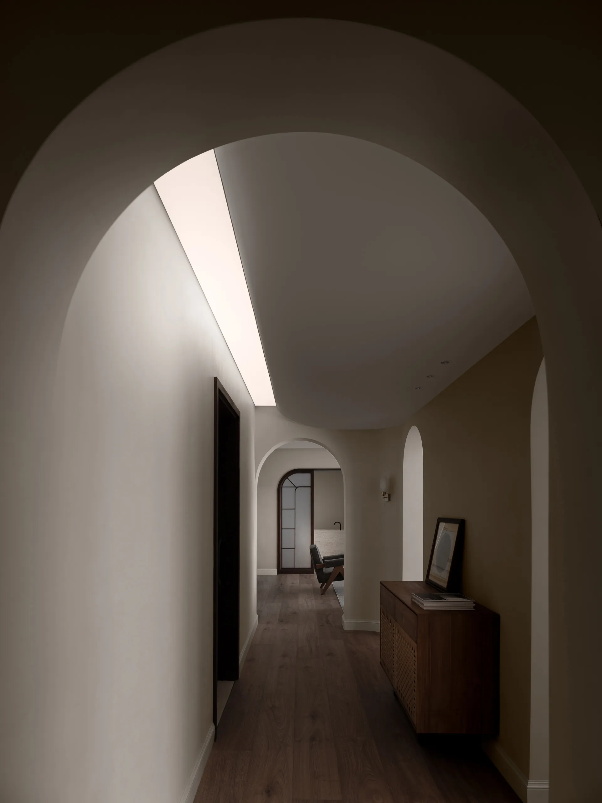 A minimalist hallway with arched doorways and warm, neutral colors.
