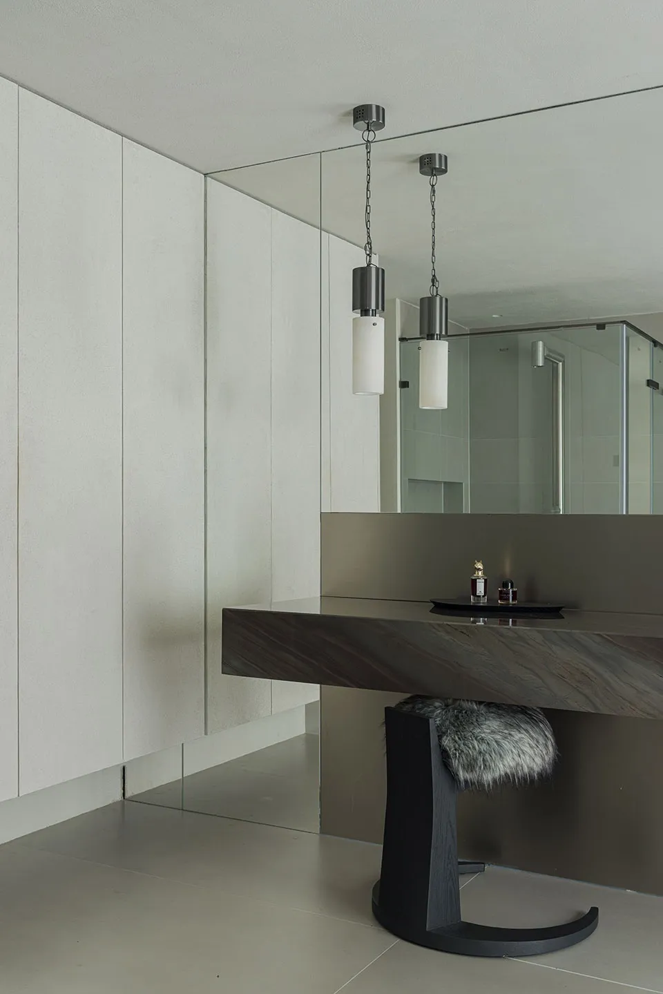 Modern minimalist bathroom featuring a sleek, concrete vanity with a glass shower enclosure, geometric shapes, and a fur stoo