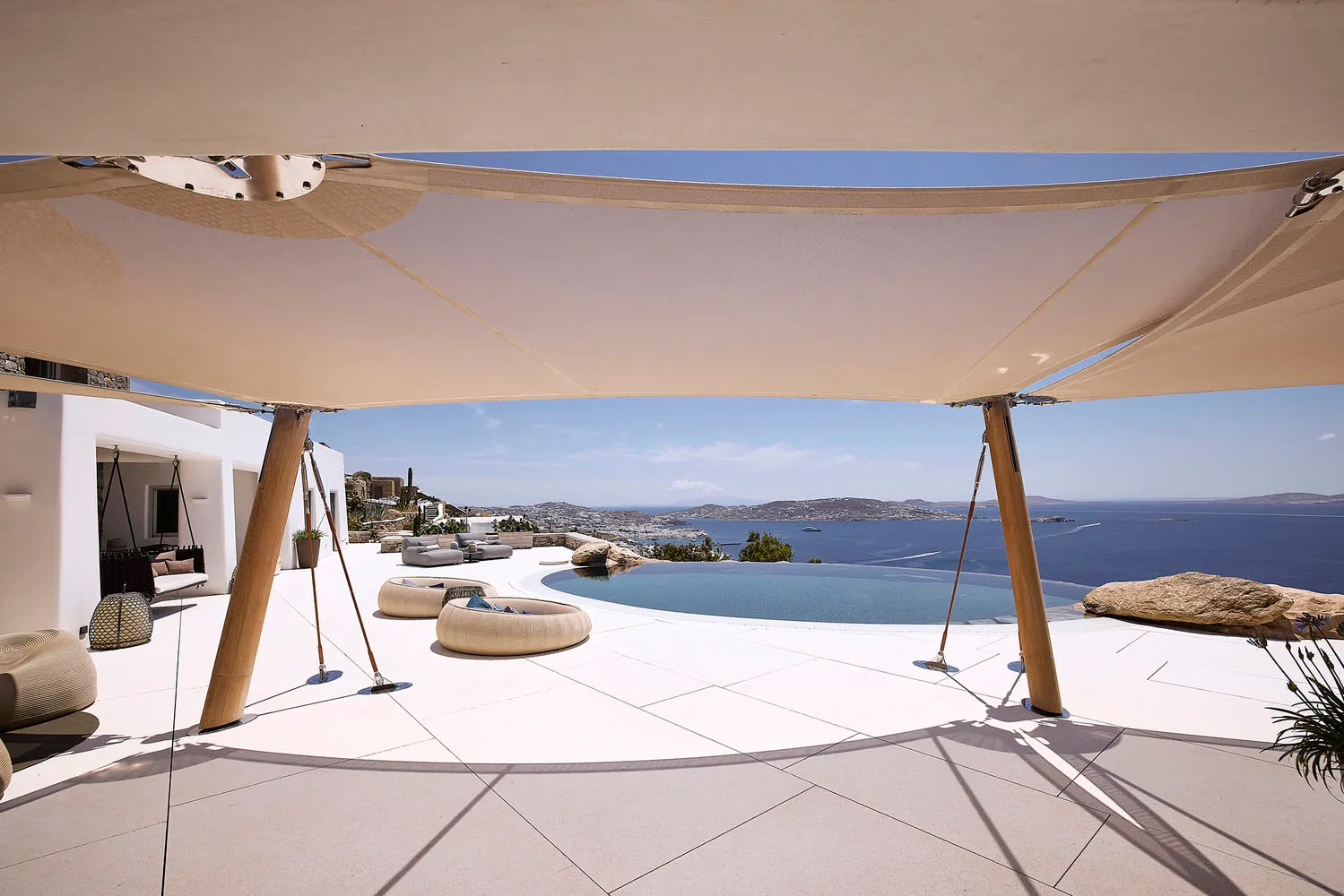 A modern residential patio featuring concrete flooring, a circular seating area, an infinity pool, and scenic ocean views.