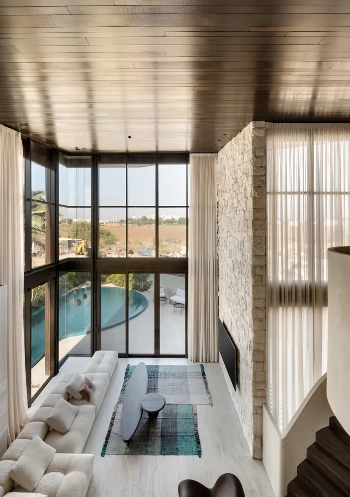 A modern living room with large glass windows, a stone wall, and a plush white sofa.