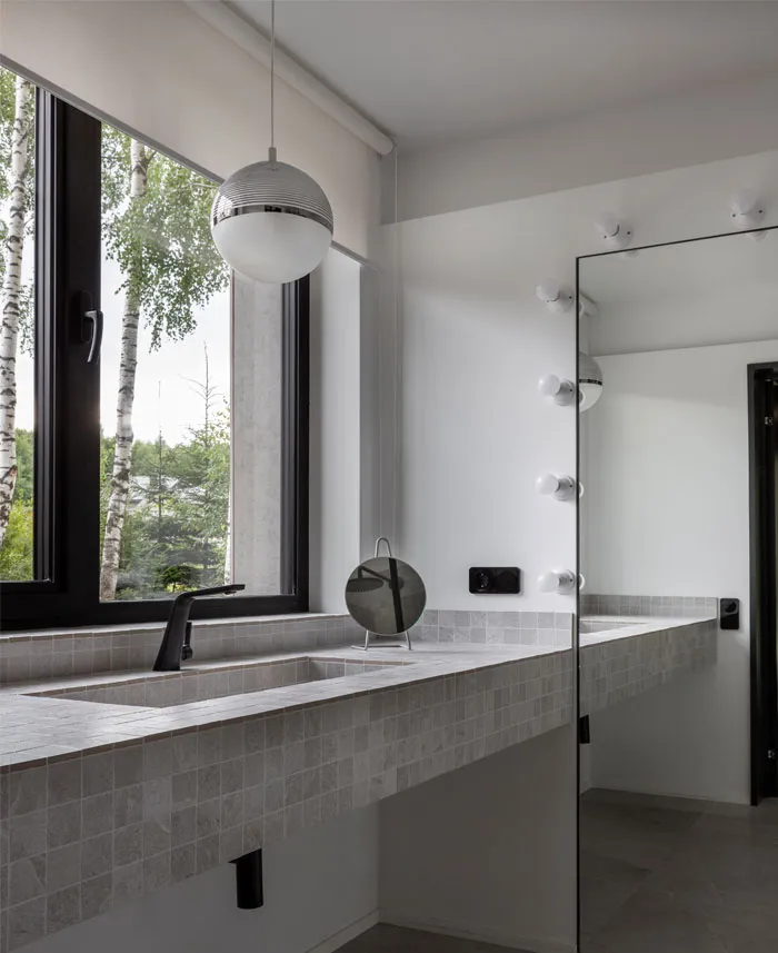 Modern bathroom interior with tiles and marble accents, featuring a large window with a view of trees.