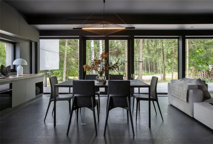 Modern minimalist dining room featuring black metal table and chairs with large windows showcasing natural forest view.