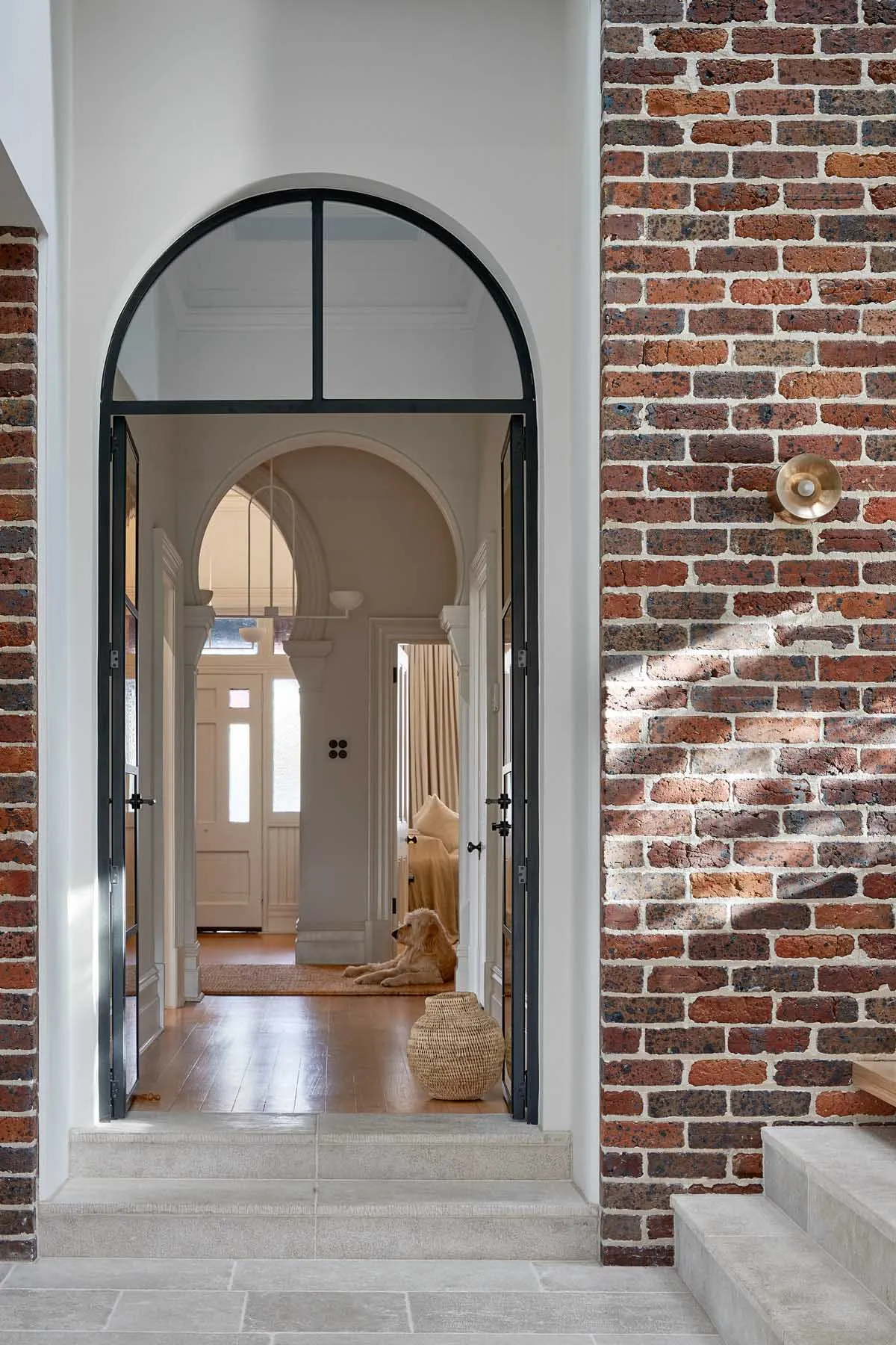 Architectural entryway with brick walls and wooden flooring, featuring a dog sitting on a rug.