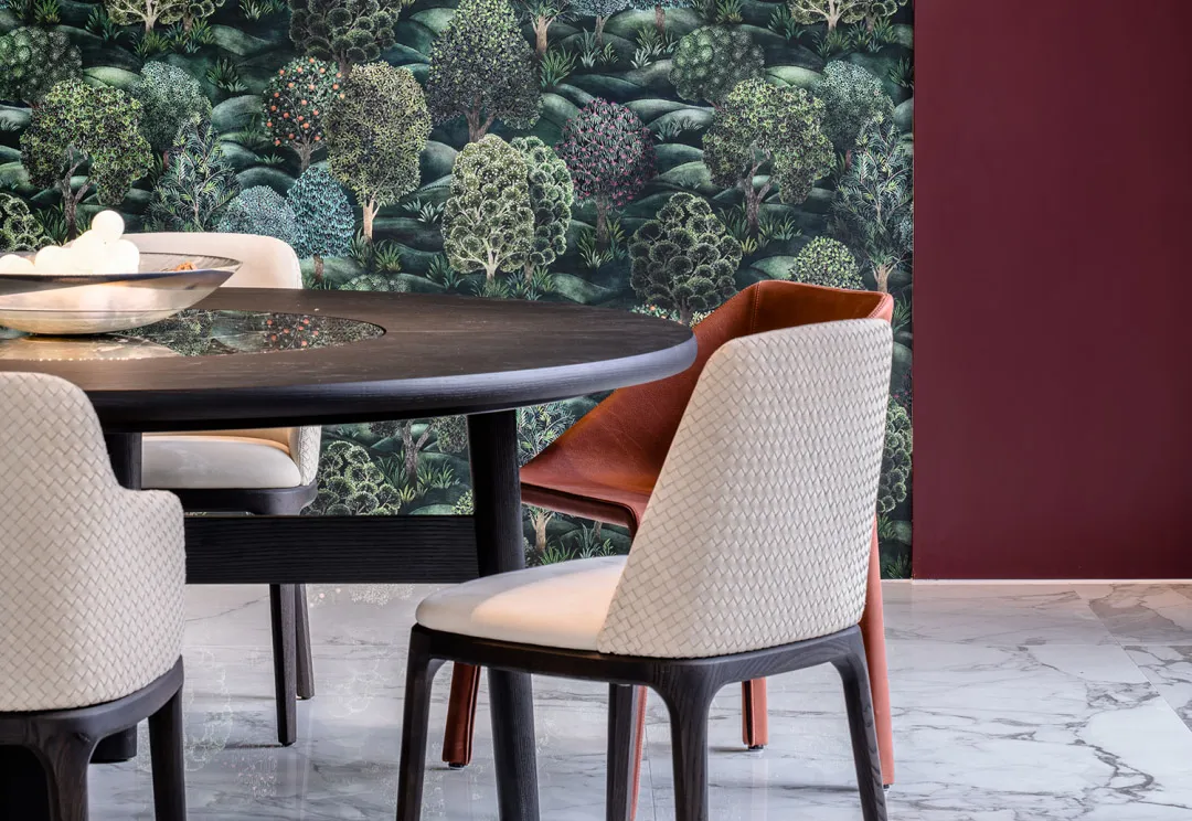 Modern dining area featuring a wooden table and upholstered chairs with a textured design against a wallpaper with tree patte
